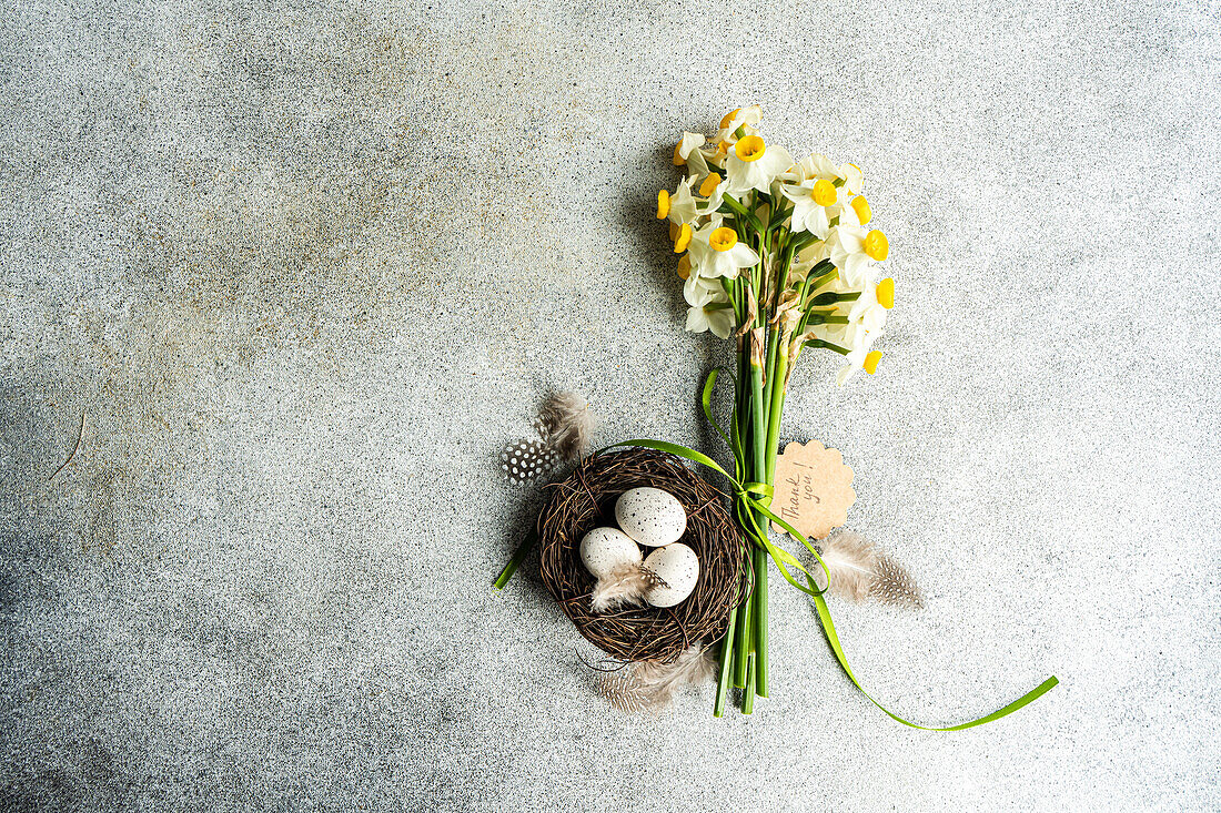 Osterkartenkonzept von oben mit Nest mit Eiern und Narzissenblüten im Strauß
