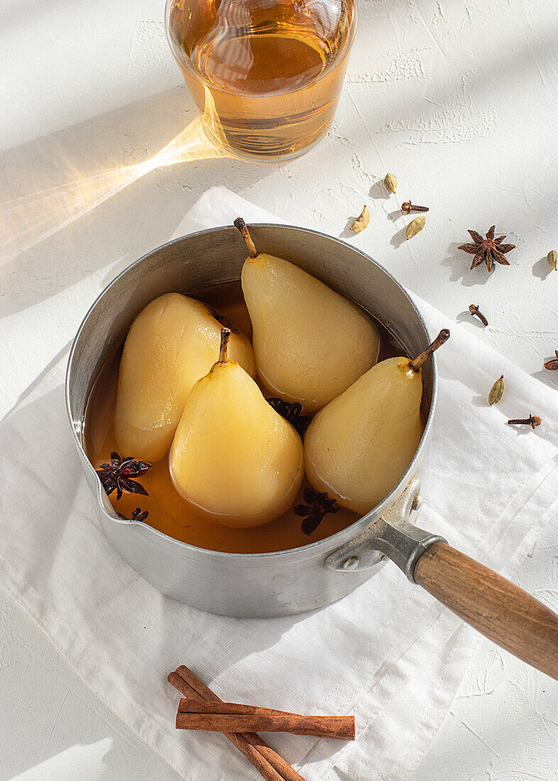 From above saucepan with delicious poached pears in white wine at table near star anise and jar with juice