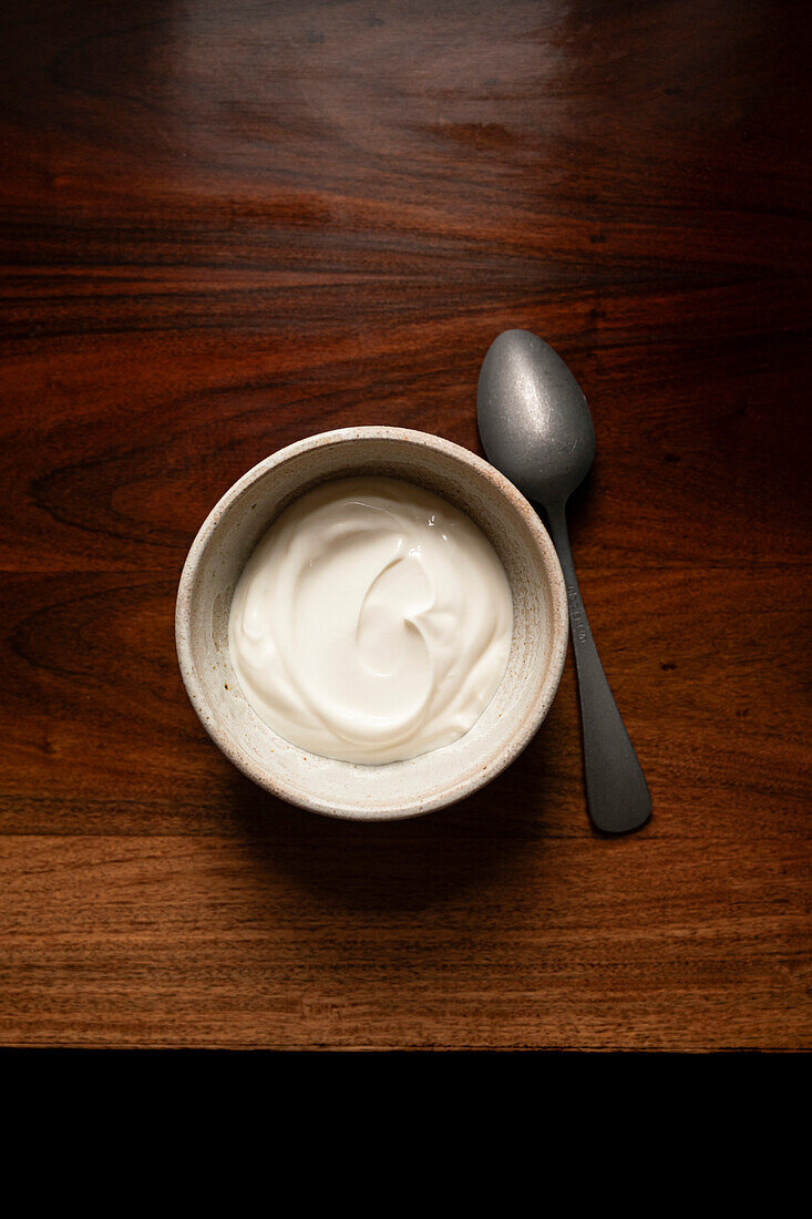 Bowl of yoghurt on an antique wooden table with silver spoon