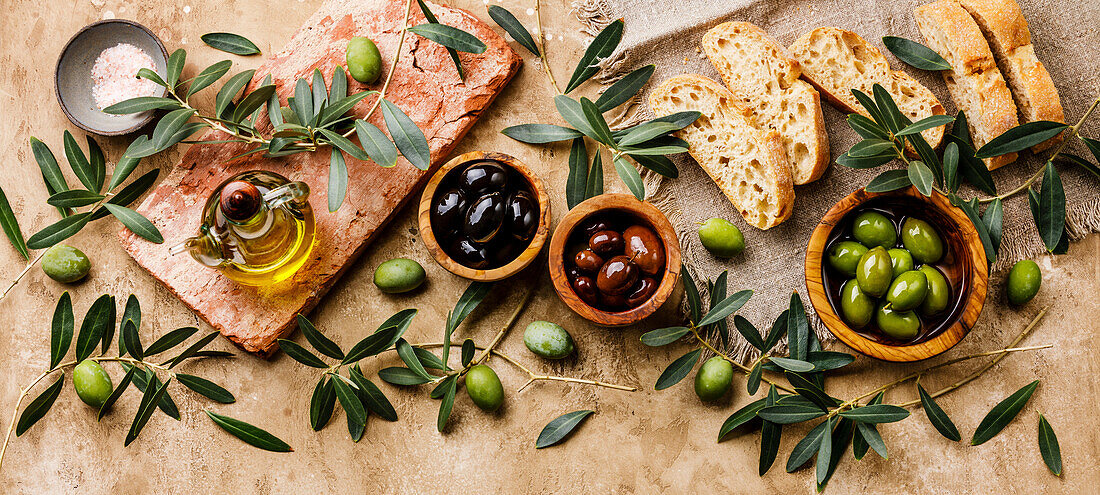 Italian food with olives, sliced ciabatta bread and olive oil on a travertine background
