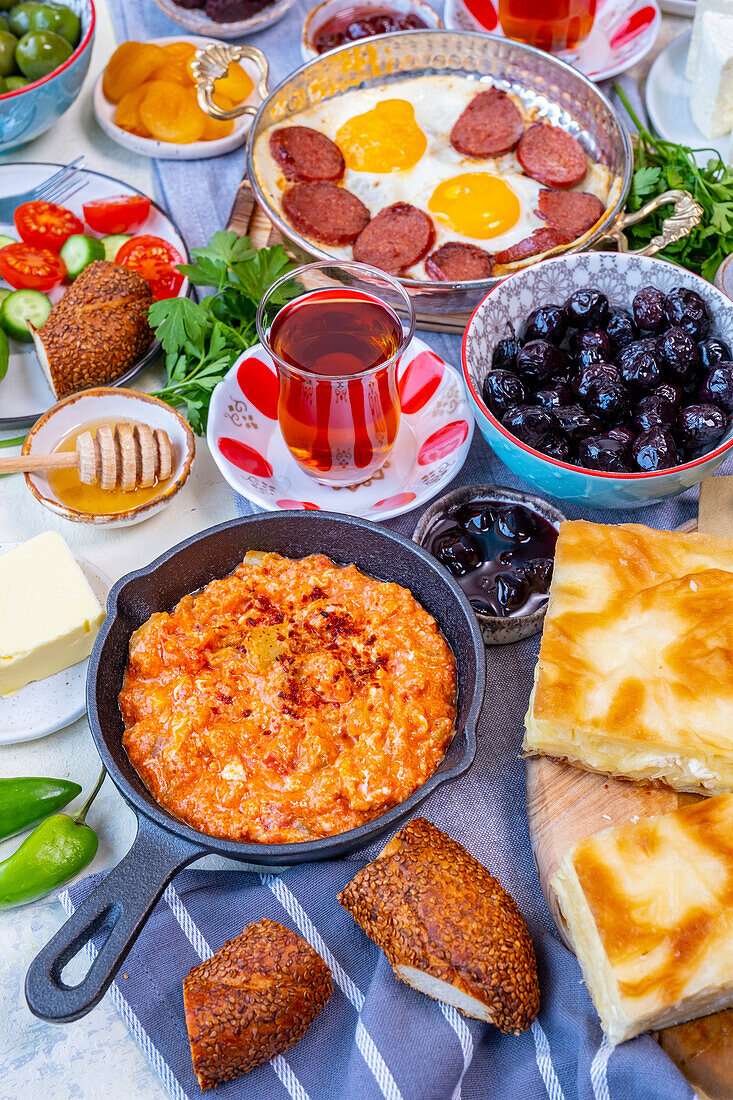 Türkisches Frühstück mit Menemen, Eiern und Sujuk, Oliven, Marmelade, Simit, Borek, Butter, Honig, Salat und türkischem Tee