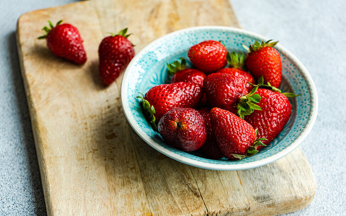 Ripe organic strawberries in ceramic bowl on concrete background