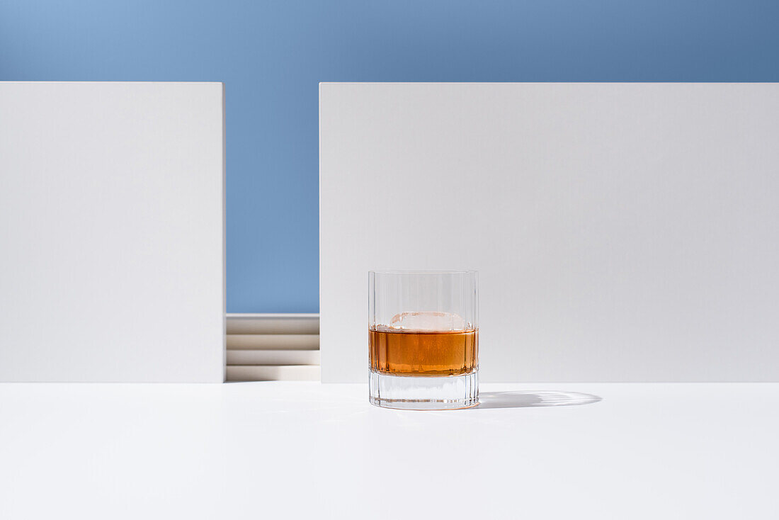 Kristallklares Glas, gefüllt mit Whiskey, auf weißer Fläche vor weißen Wänden