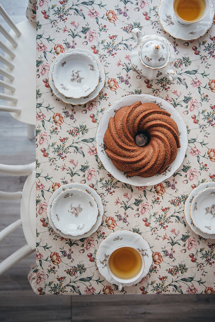 Ein veganer Kuchen auf einem Blumentisch mit Tassen Tee