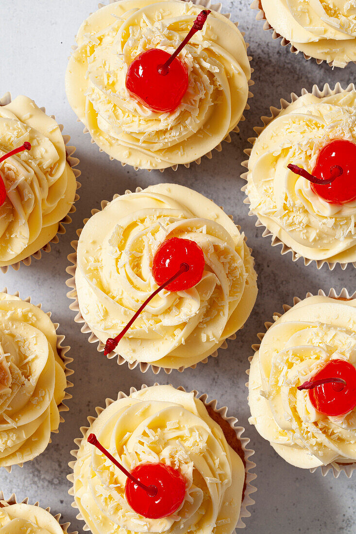 Draufsicht auf Cupcakes mit gespritzter Buttercreme, weißen Schokoladenraspeln und Maraschino-Kirschen