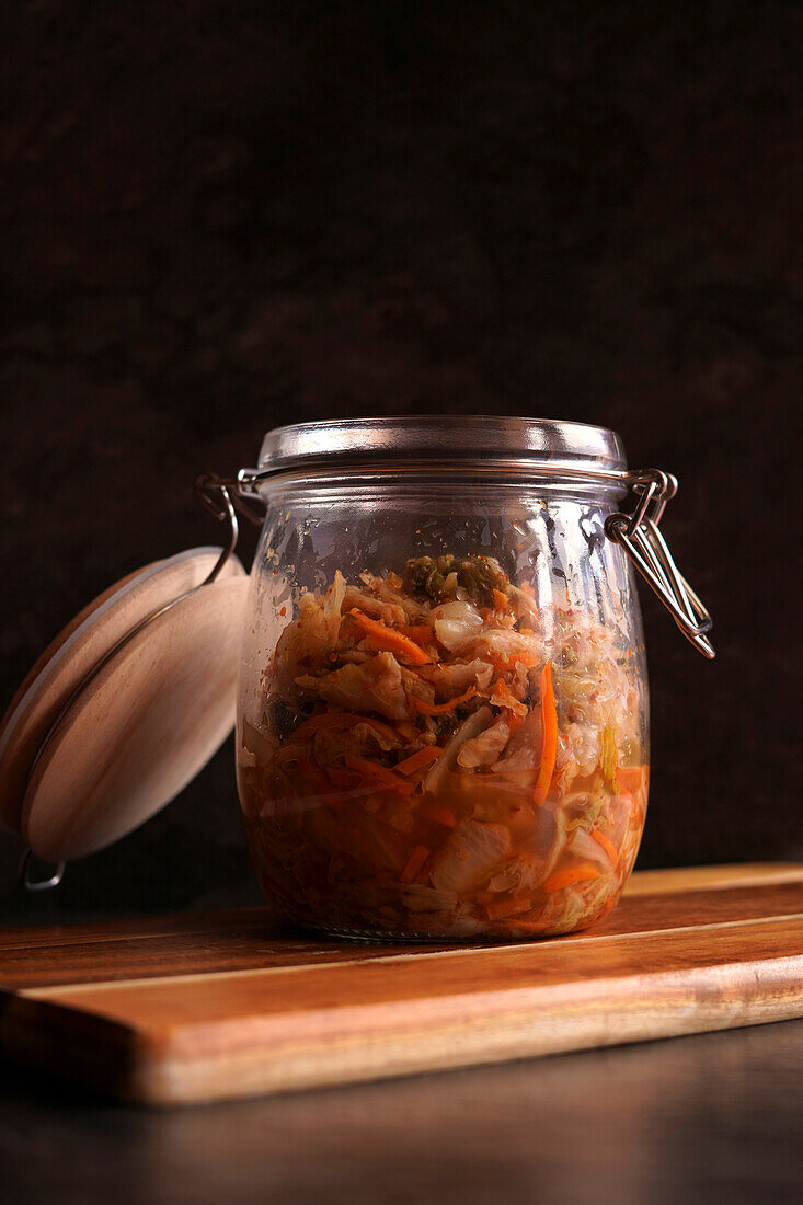 Healthy probiotic Korean style Kimchi in glass jar close up with negative copy space, against a dark background.