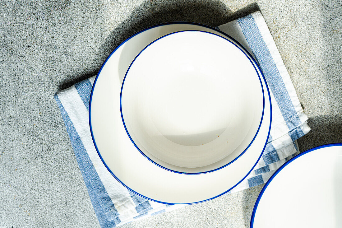 Draufsicht auf einen minimalistisch-rustikal gedeckten Tisch mit weißen Tellern und gestreifter Serviette auf grauer Fläche im Tageslicht
