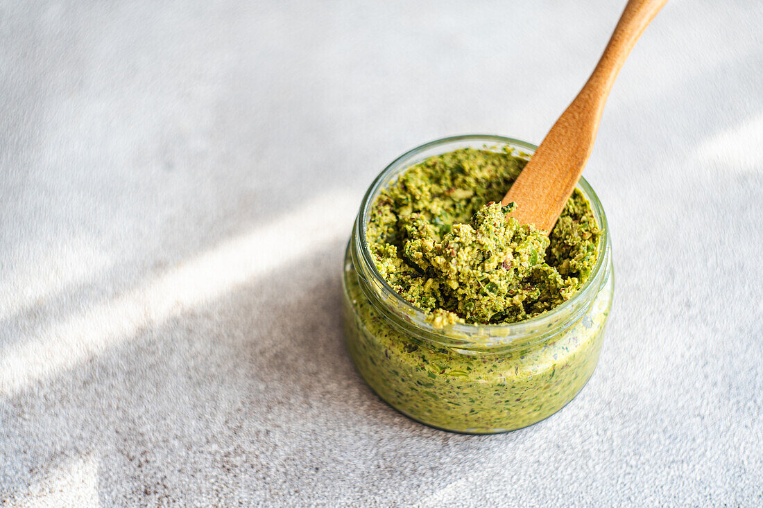 From above of fresh green pesto sauce and wooden spoon placed on table during preparation for healthy meal at home
