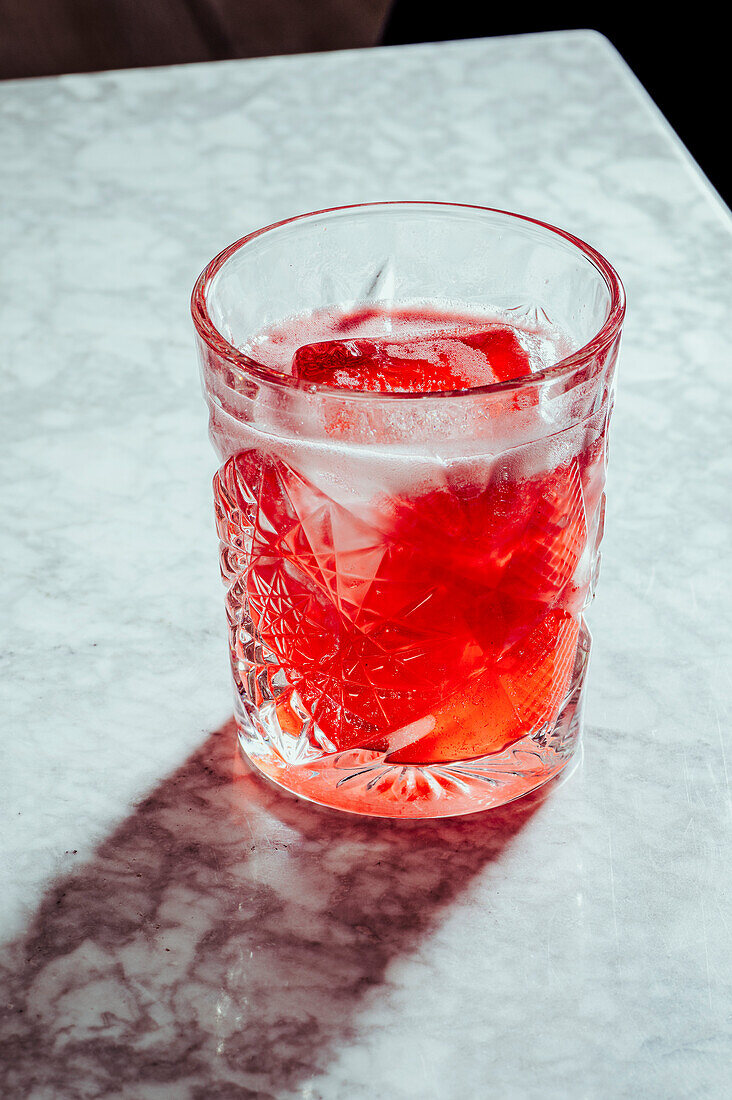 Hoher Blickwinkel auf einen erfrischenden Alkoholcocktail mit Eiswürfeln im Glas auf einer Marmortheke