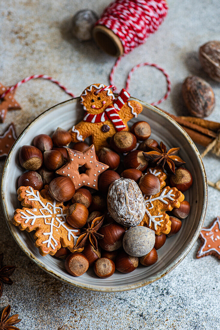 Top view of plate of heap of chestnuts with tasty Christmas cookies placed on table near spool of red thread