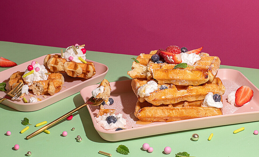 From above tasty sweet waffles topped with berries fruits sauce and cream served on pink tray on colorful table background in light kitchen