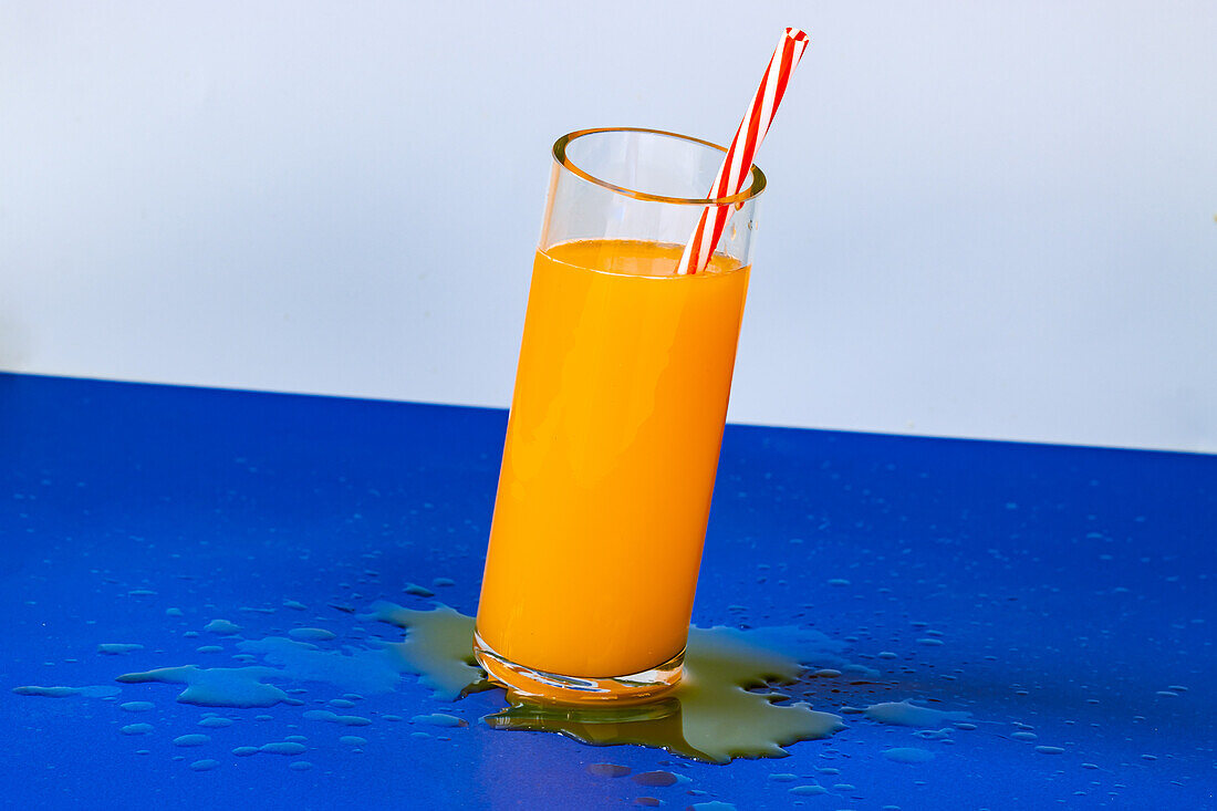 Close up shot of glass of fresh orange juice cocktail with spill on blue background