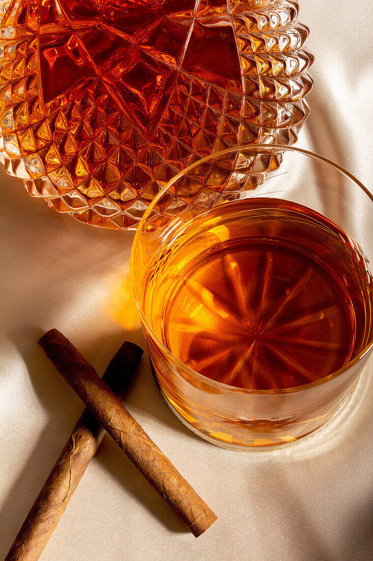 Top view of glass of whiskey placed on table near decanter and cinnamon sticks