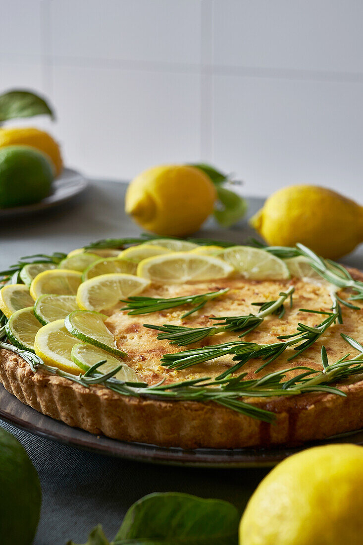Round lemon pie with decorated with lemon slices and rosemary sprigs on table in the kitchen