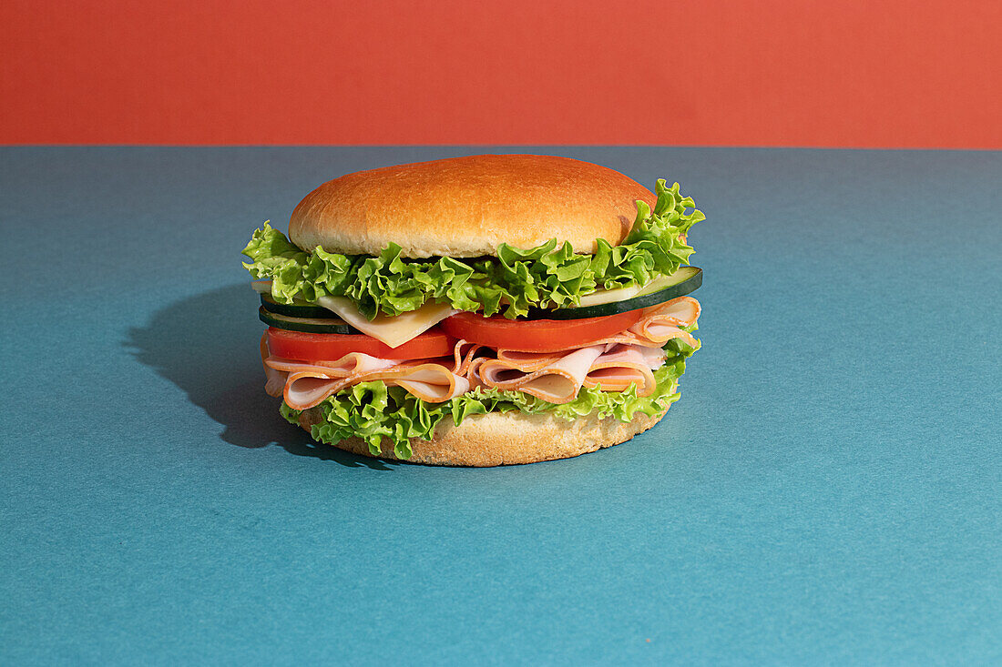 Delicious sandwich with ham, tomatoes, cucumber and cheese slices and fresh lettuce on blue and orange background