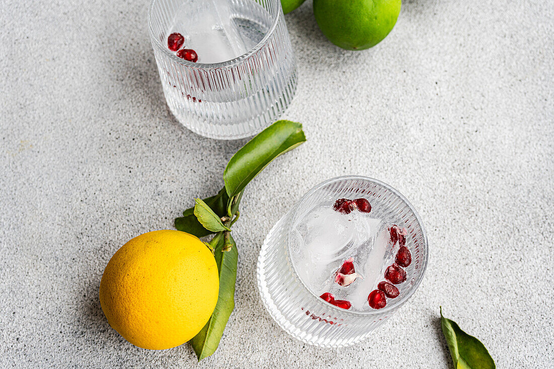 A sophisticated gin tonic cocktail with lemon and red berries, served on a textured surface with fresh citrus in view.