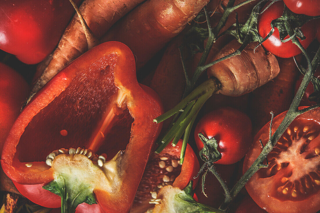 Lebensmittel-Hintergrund mit Nahaufnahme von rohem orangefarbenem und rotem Gemüse: Paprika, Karotten und Tomaten. Gesunder Lebensstil mit vitaminreichen Zutaten. Ansicht von oben