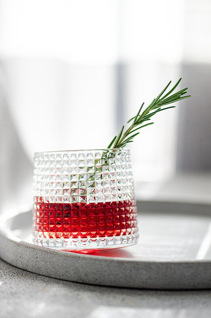 Eleganter Cocktail mit Kirsch- und Apfelsaft, gemischt mit Wodka, garniert mit einem frischen Rosmarinzweig, präsentiert auf einem runden Tablett