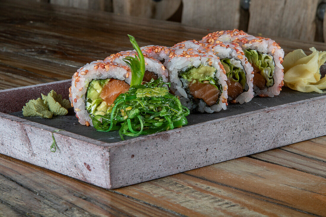 Closeup of served set of avocado tuna uramaki sushi rolls with wakame salad on side on concrete plate