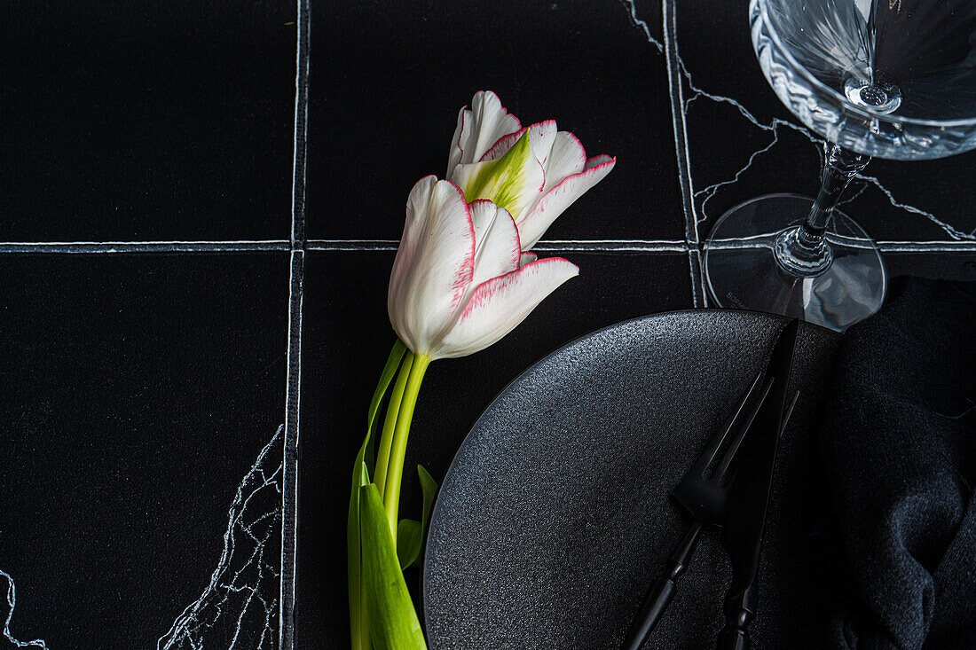 Draufsicht auf einen gedeckten Tisch mit frischen Tulpenblüten auf schwarzem Betonhintergrund