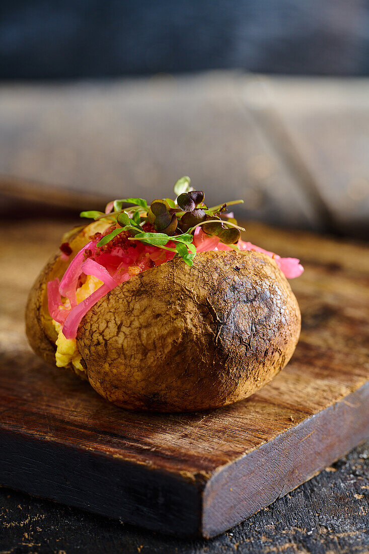 Appetitliche traditionelle ecuadorianische Kumpir-Kartoffel mit Füllung und Kräutern auf einem hölzernen Schneidebrett vor einem unscharfen Hintergrund