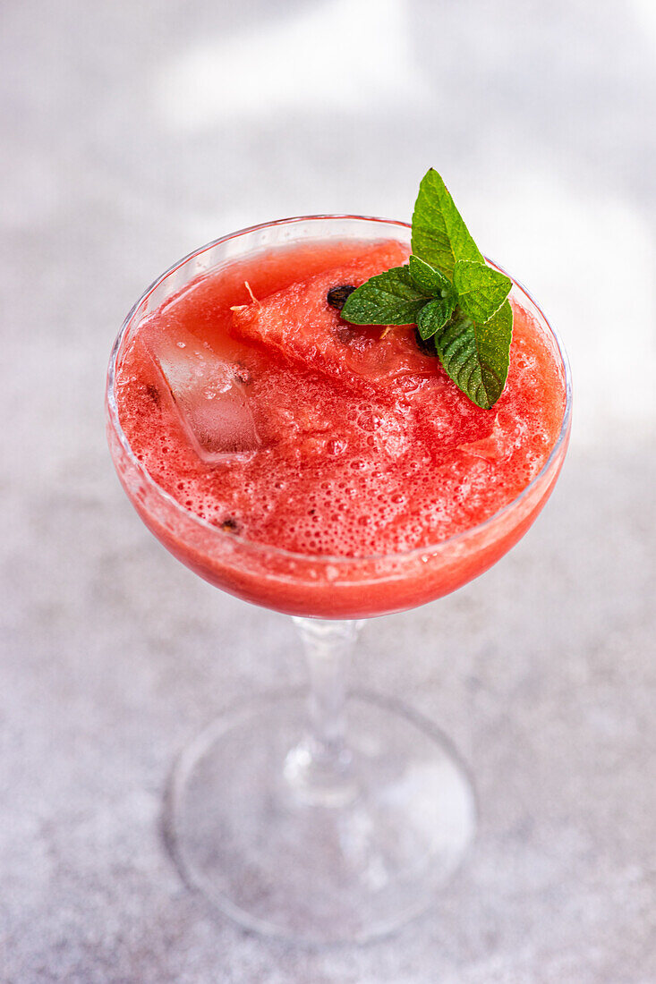 Top view of cup of fresh Margarita cocktail with watermelon smoothie covered with mint leaves