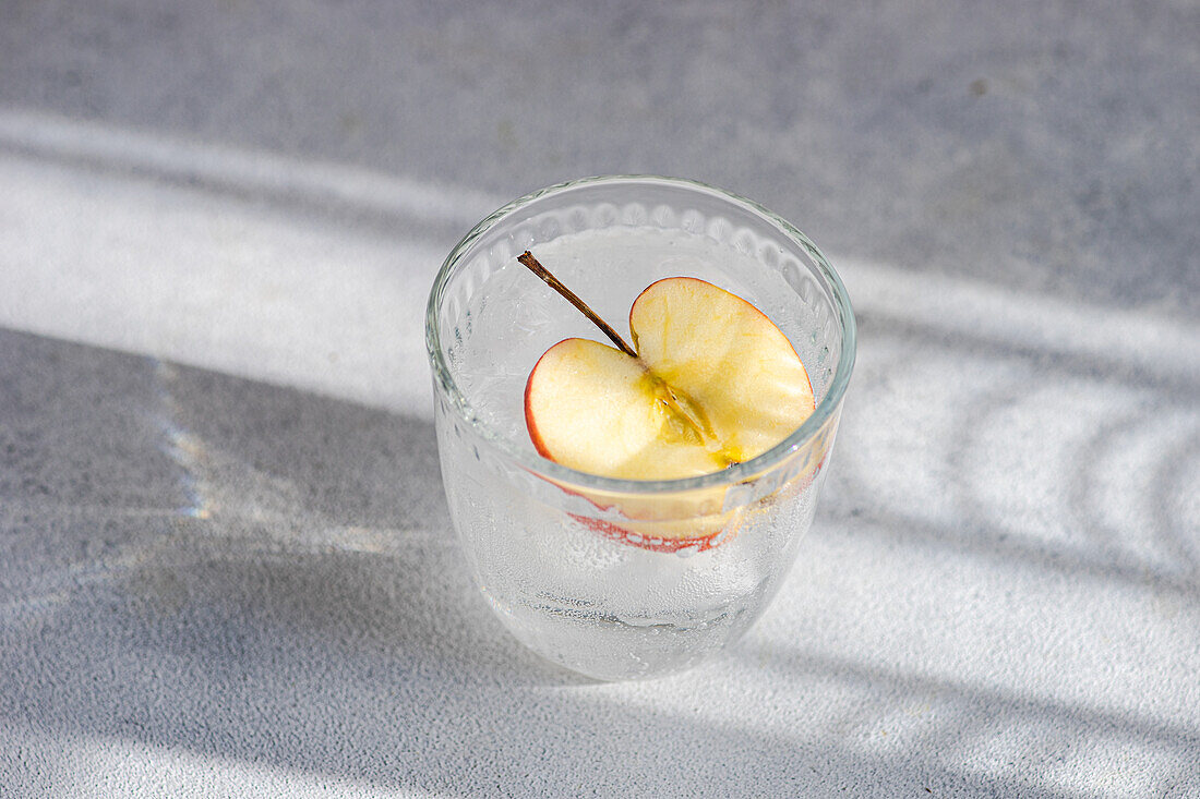 Von oben gesehenes Glas Tonic Water mit einer Apfelscheibe, mit weichen Schatten und hellen Texturen im Hintergrund