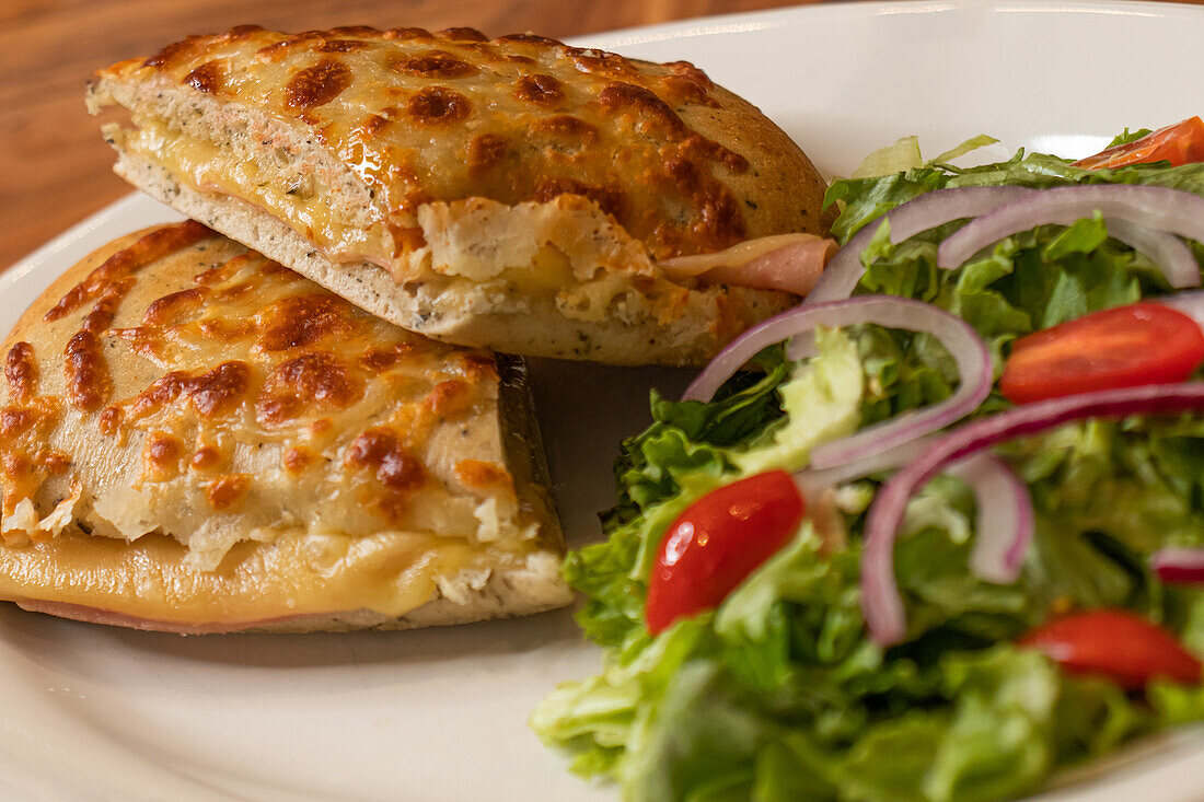 Appetitliche gebackene Chapatas mit gemischtem Salat aus Tomaten, Zwiebeln und grünem Salat, serviert auf einem weißen Marmorteller auf einer hölzernen Oberfläche im Licht