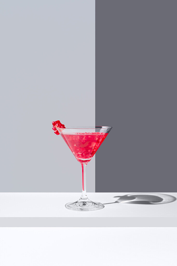 Glass filled with red pomegranate cocktails served with pomegranate seeds against a gray backdrop, casting a soft shadow