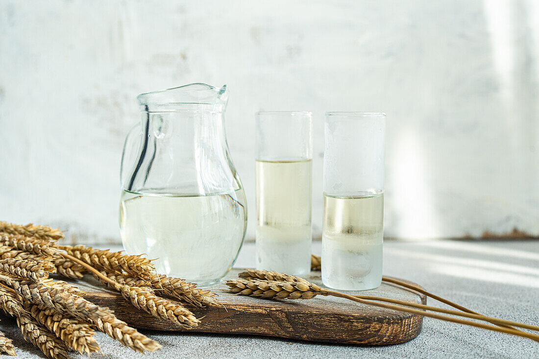Traditional Ukrainian alcoholic drink made from wheat and known as Gorilka served in transparent jar and glasses placed on cutting board against blurred background