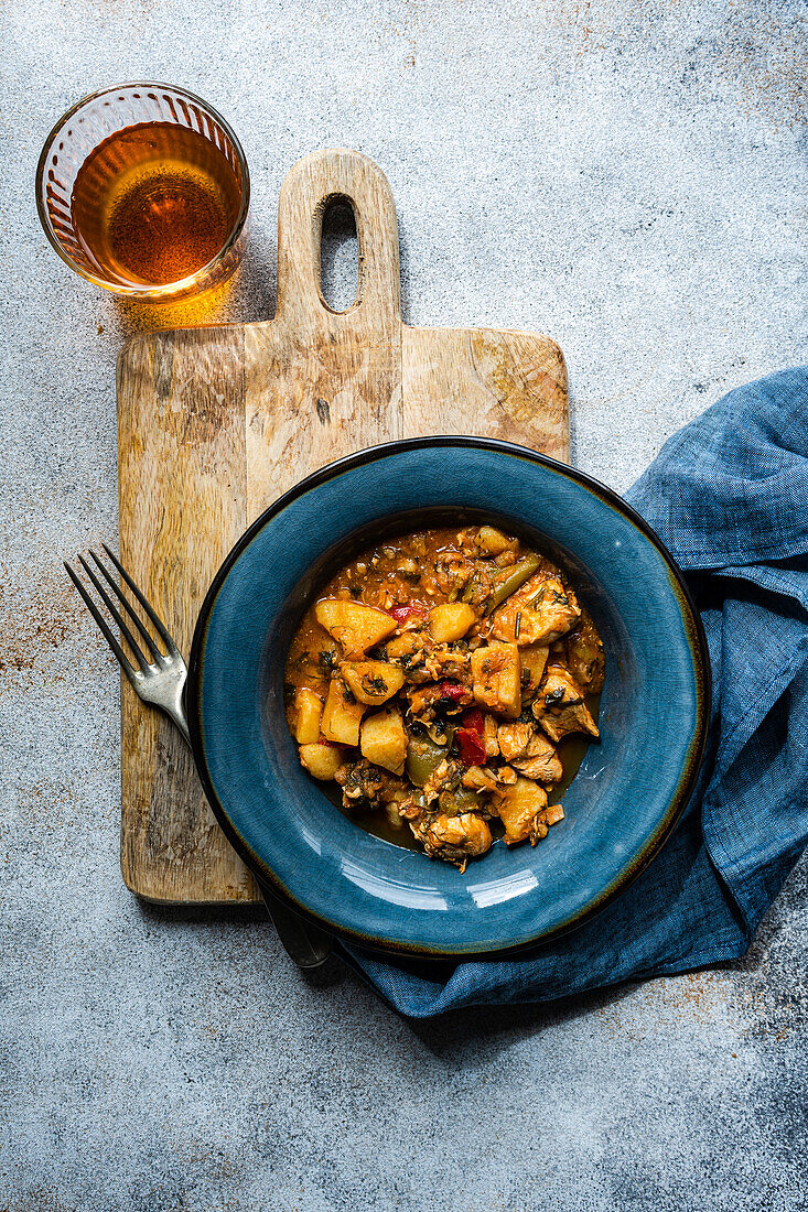 Top view of a chicken meat stew with vegetables served in the ceramic bowl and glass of amber wine