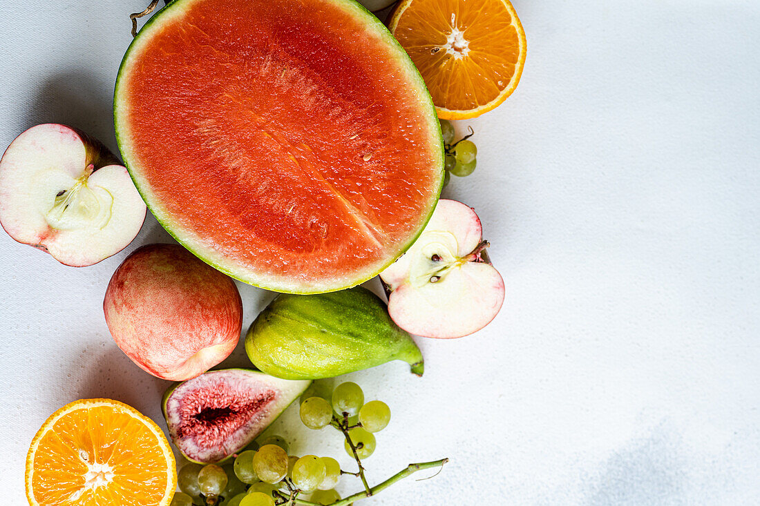 Draufsicht auf einen Rahmen mit Früchten der Saison, bestehend aus Wassermelone, Orange, Birne, Weintrauben und Äpfeln, auf einer weißen Fläche