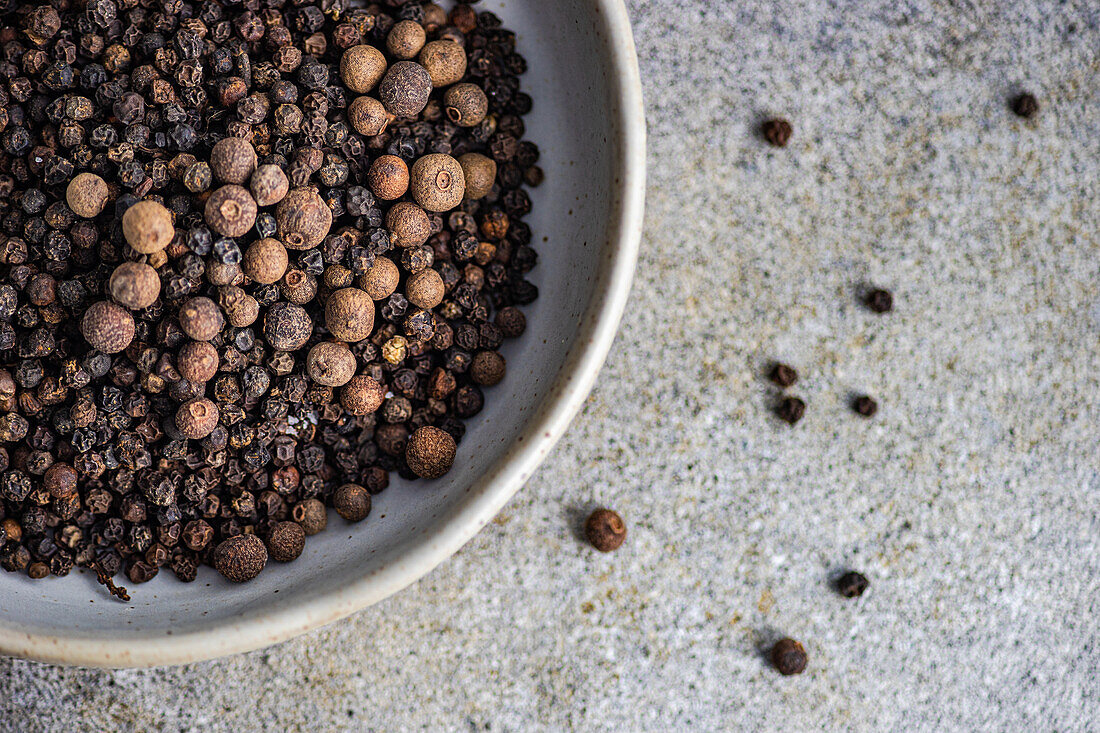 Top view of crop bowl filled with natural aromatic Black pepper in grain on grey concrete background