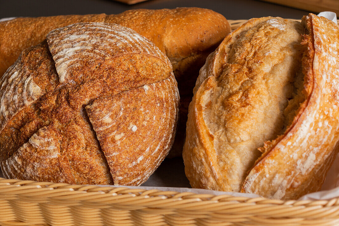 Focused of various tasty freshly baked pastry breads being served with baking pan into wicker basket with fabric on dining table indoors