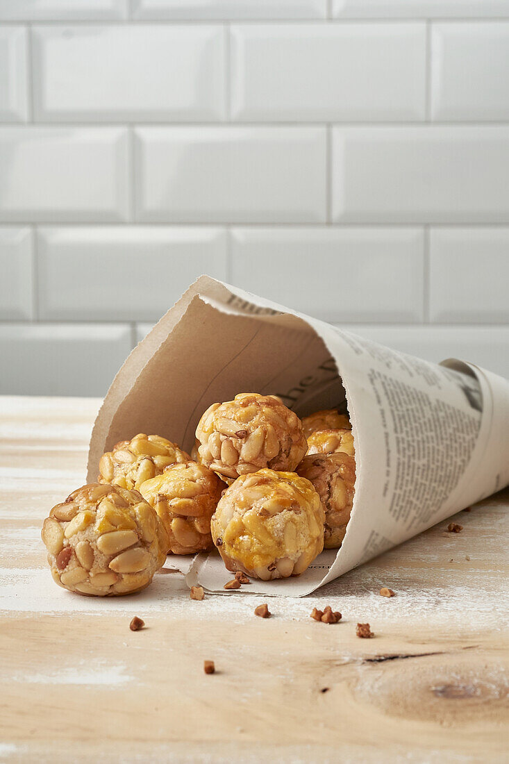 Sweet panellets in newsprint cone placed on wooden table against white tile wall