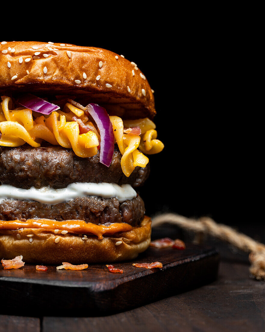 Nahaufnahme von geerntetem Hamburger mit Makkaroni und Käse auf einem Holztablett auf einem Tisch vor dunklem Hintergrund