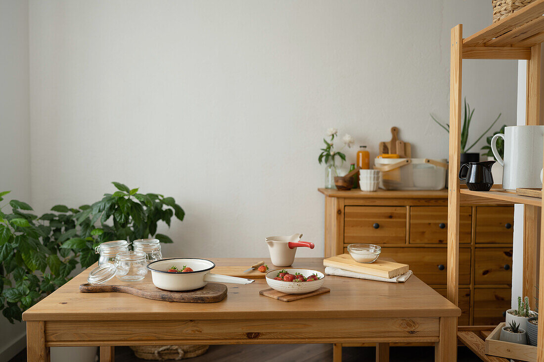 Esstisch aus Holz mit Bechern und Schale mit Erdbeeren, bereit für die Zubereitung von Erdbeermarmelade zu Hause