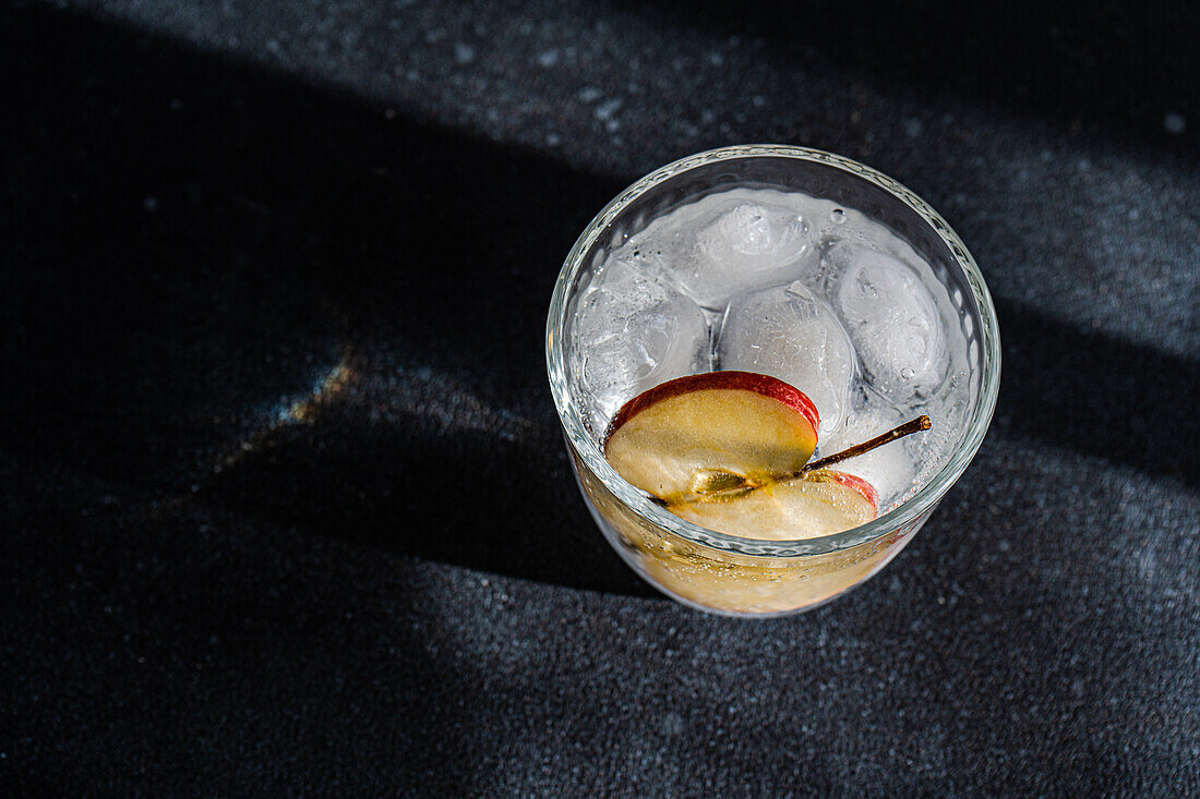 Tonic Water mit einer Apfelscheibe in einem Glas vor einem dunklen, stimmungsvollen Hintergrund mit dramatischer Beleuchtung von oben