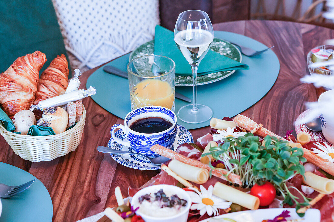 A well-appointed brunch table featuring a variety of foods including fresh croissants, cold cuts, and cheese, accompanied by coffee, juice, and wine.