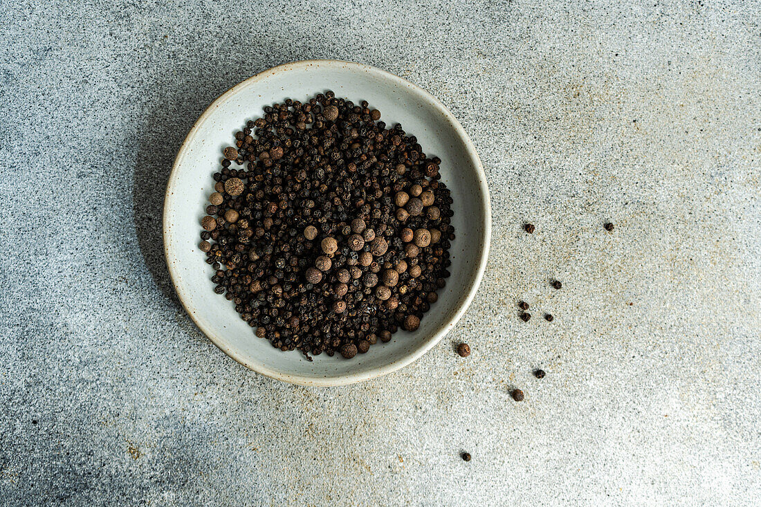 Top view of bowl filled with natural aromatic Black pepper in grain on grey concrete background