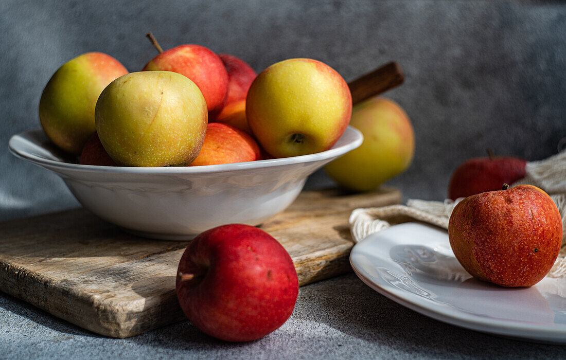 A collection of ripe, colorful apples presented on a rustic wooden board, with a white plate and draped fabric creating a serene kitchen setting