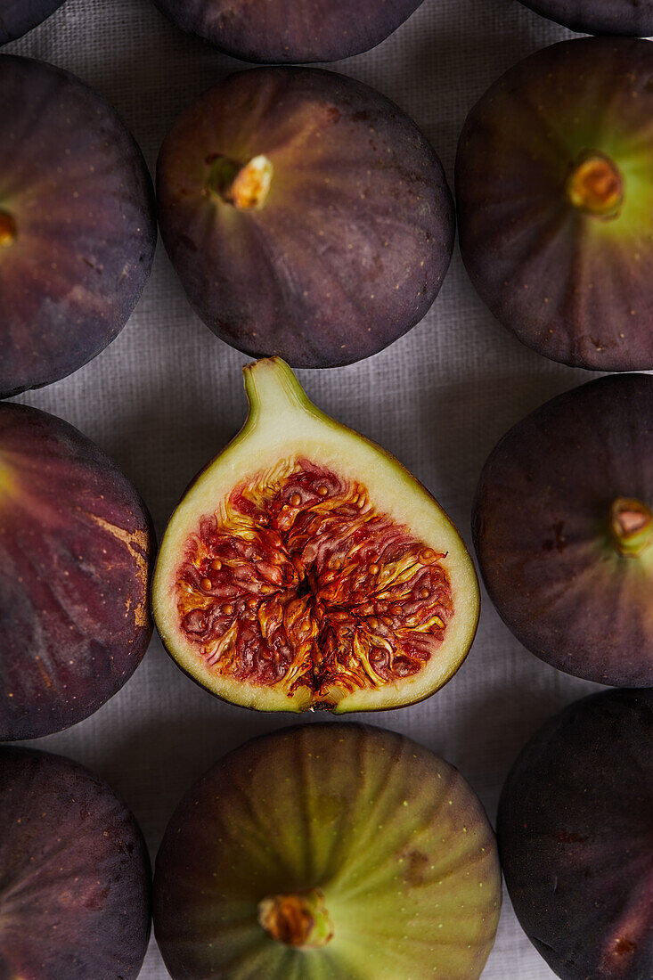 Top view of closeup of minimalist composition with half sweet fig placed on gray napkin surrounded by fresh figs