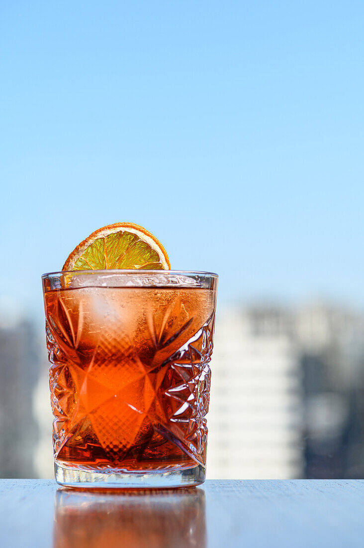Appetitanregender erfrischender alkoholischer Negroni-Cocktail mit Orangenscheibe und Eiswürfel im Glas auf einem Tisch in einer Bar mit unscharfem Hintergrund