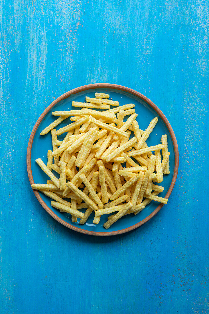 Top view of ceramic plate with French fries placed on blue surface
