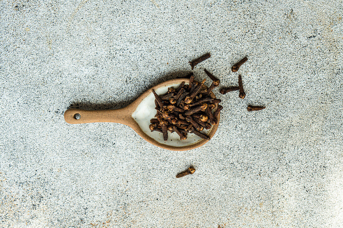 Top view composition with wooden spoon with cloves placed on concrete table in blurred background