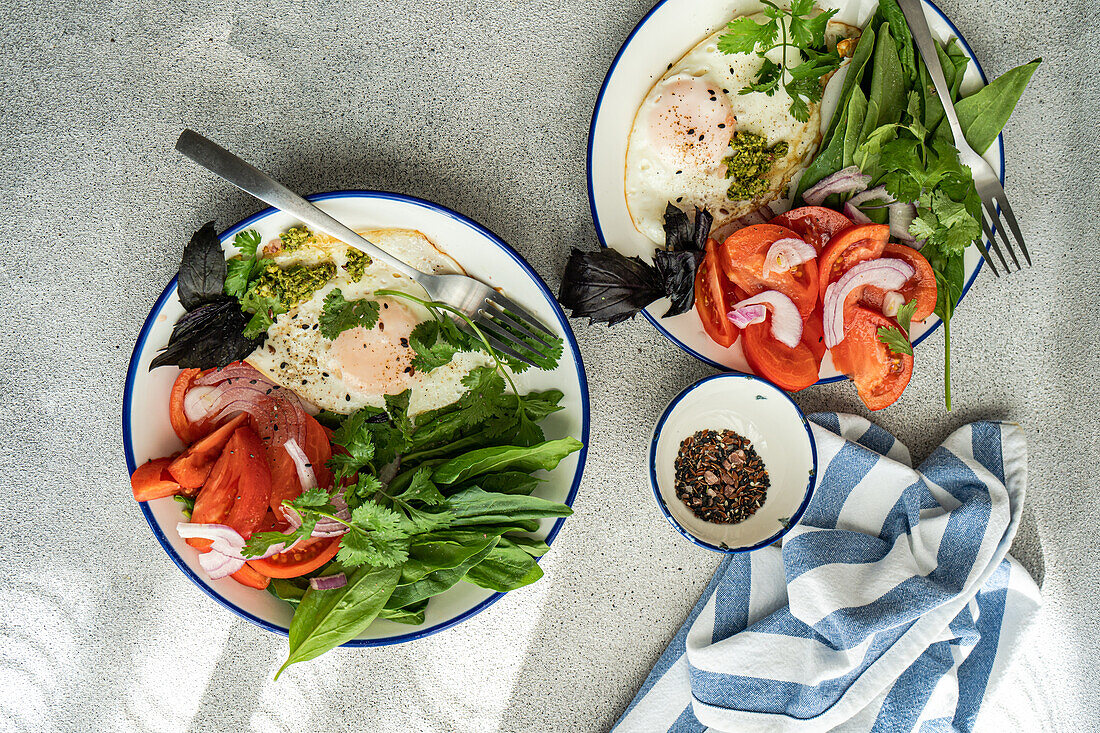 Two bowls filled with keto-friendly ingredients including leafy greens, eggs, and tomatoes on a textured counter.
