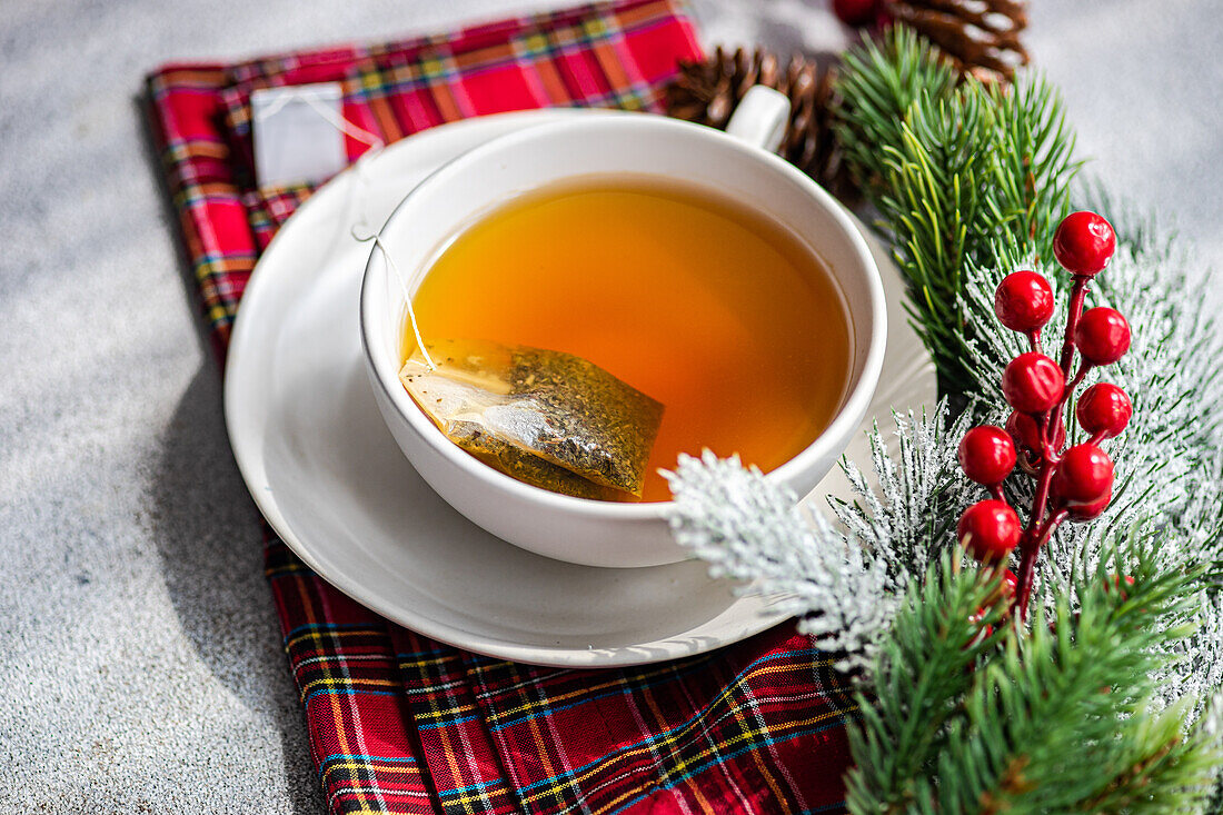 Hohe Winkel von Weihnachten Tasse Tee auf rote Serviette in der Nähe von Stechpalmen und Tannenzapfen auf grauen Tisch platziert