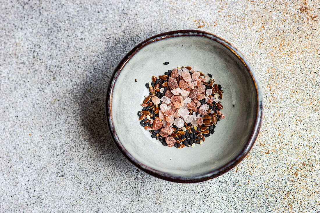 From above of bowl with salad seasoning spices mix consist of Himalayan pink salt, flax seeds, sesame seeds and black pepper on concrete background