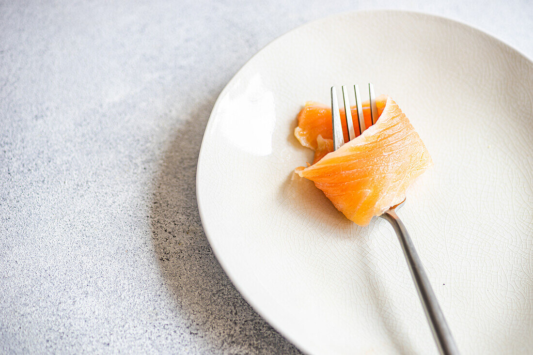 High angle of healthy salmon rolled on fork served on white plate against gray surface