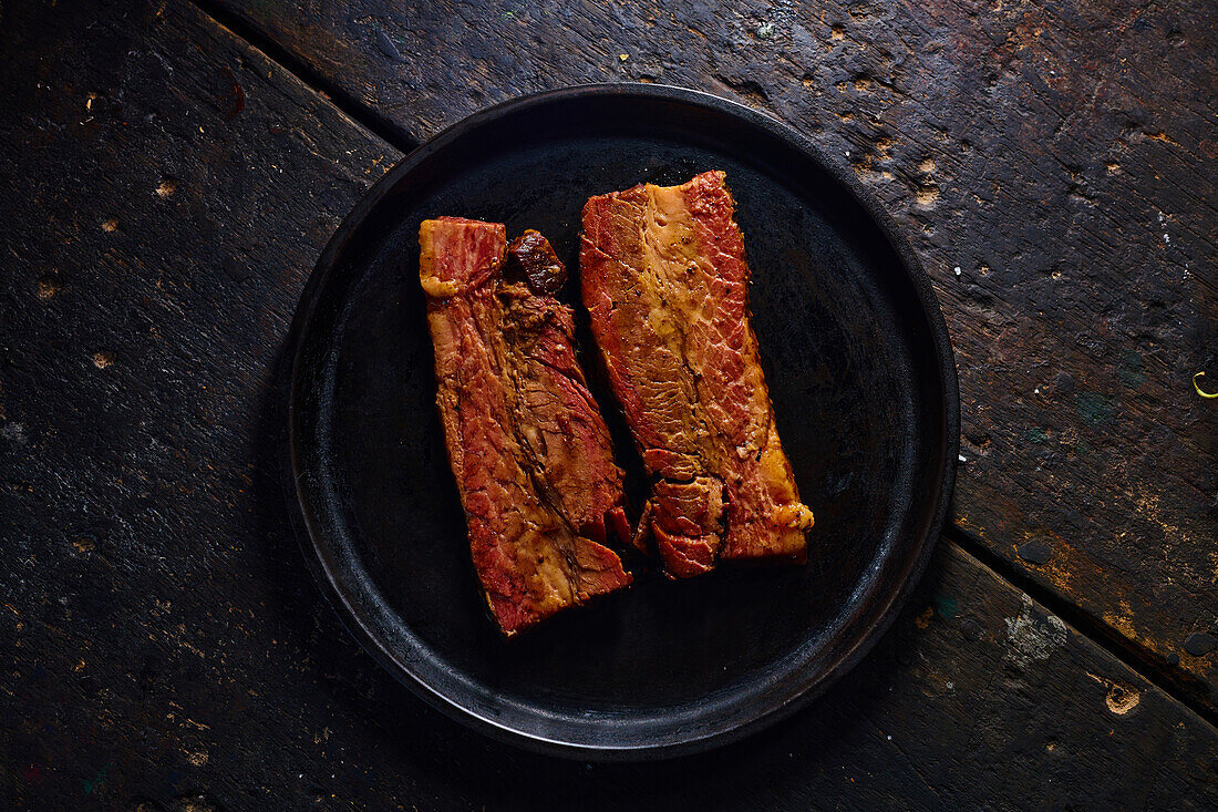 Top view of appetizing fat grilled pork ribs served on black plate placed on wooden table